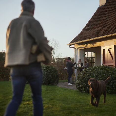 Man walking towards dog and women at winter garden party.