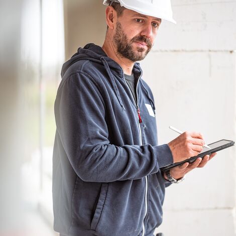 Man with white hard hat at building site holding tablet.