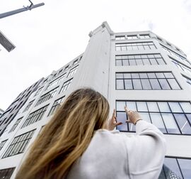 Šviesiaplaukė moteris priešais baltą vidutinio aukščio pastatą mieste